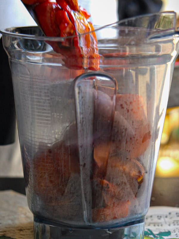 A blender pitcher filled with chunks of roasted vegetables being used.